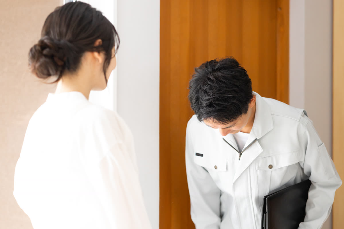 作業服の男性が玄関先で挨拶する様子