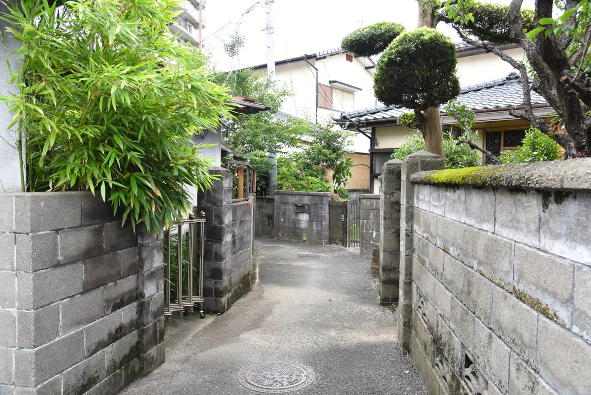 ブロック塀にはさまれた細い道と、その奥の住宅